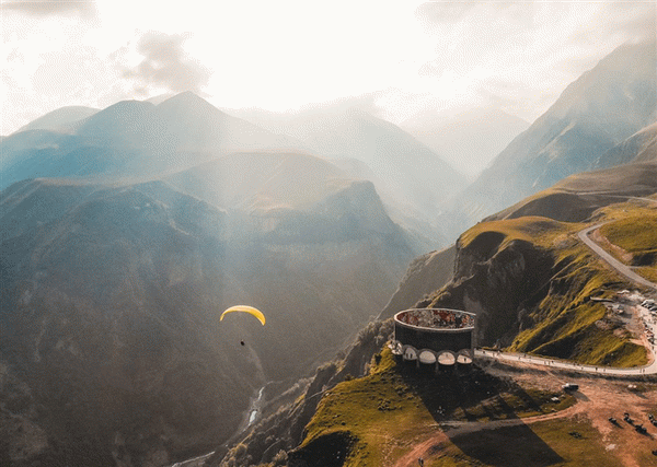 Человек прыгает с парашютом между гор